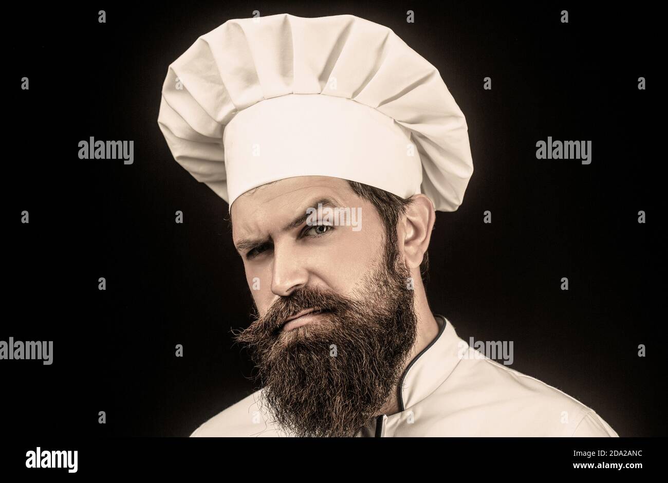 Chapeau de cuisinier. Portrait d'un cuisinier sérieux. Cuisinier barbu, cuisiniers ou boulanger. Chefs masculins barbus isolés sur du noir. Chef masculin en blanc à barbe pleine de confiance Banque D'Images