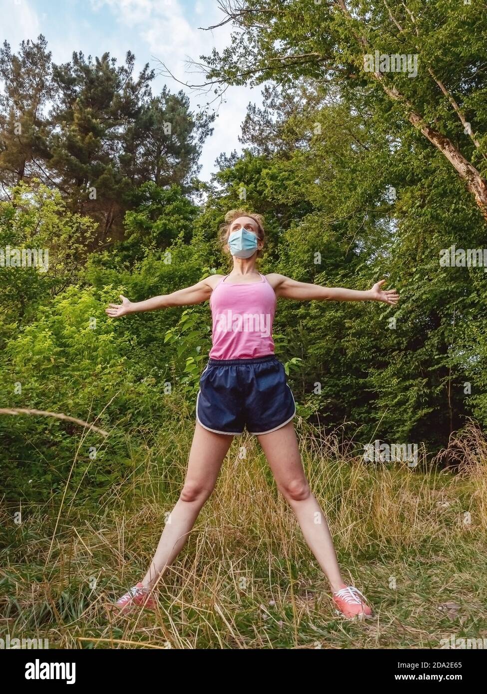 Une fille dans un masque se tient dans la forêt avec ses bras s'étirent sur les côtés et ses jambes larges à part Banque D'Images