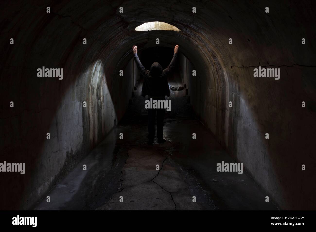 Un homme dans un tunnel souterrain sombre cherche une issue et lève les mains au ciel pour demander de l'aide. Banque D'Images