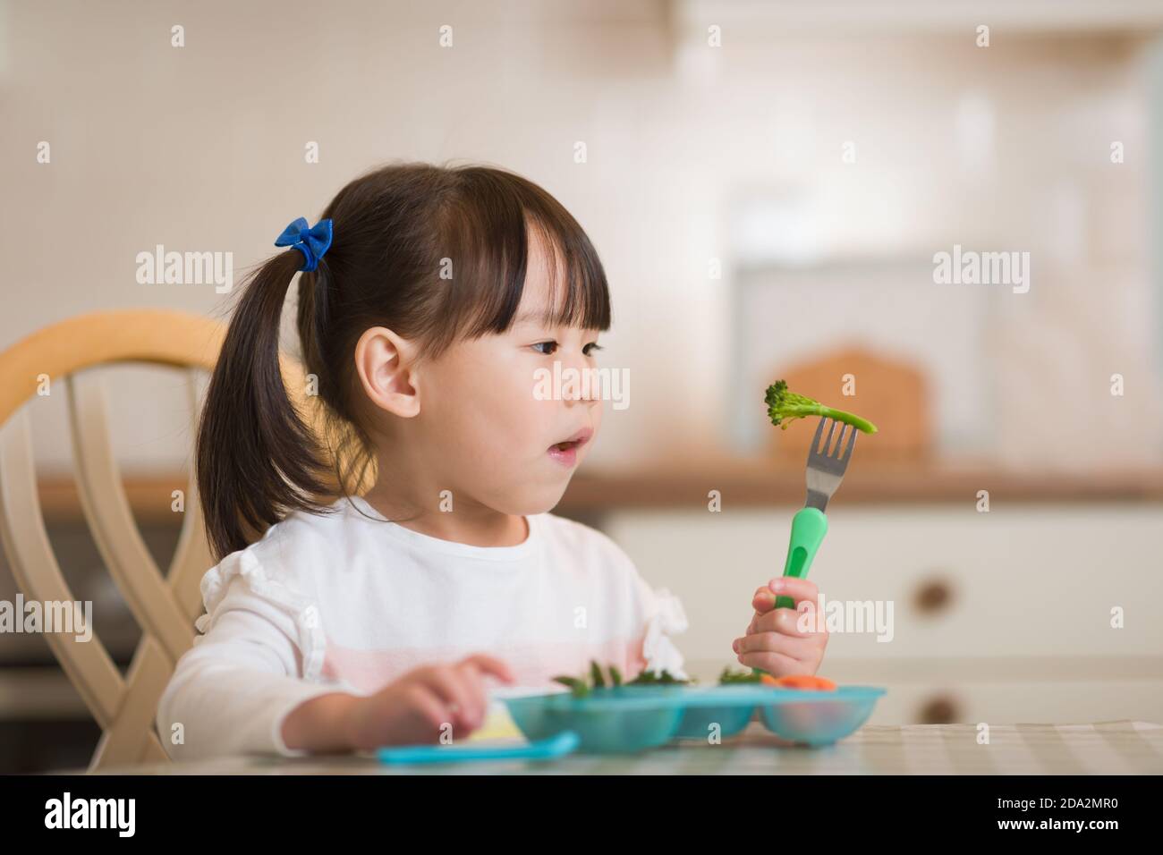 jeune fille mangeant des légumes verts frais sur fond de cuisine réel Banque D'Images