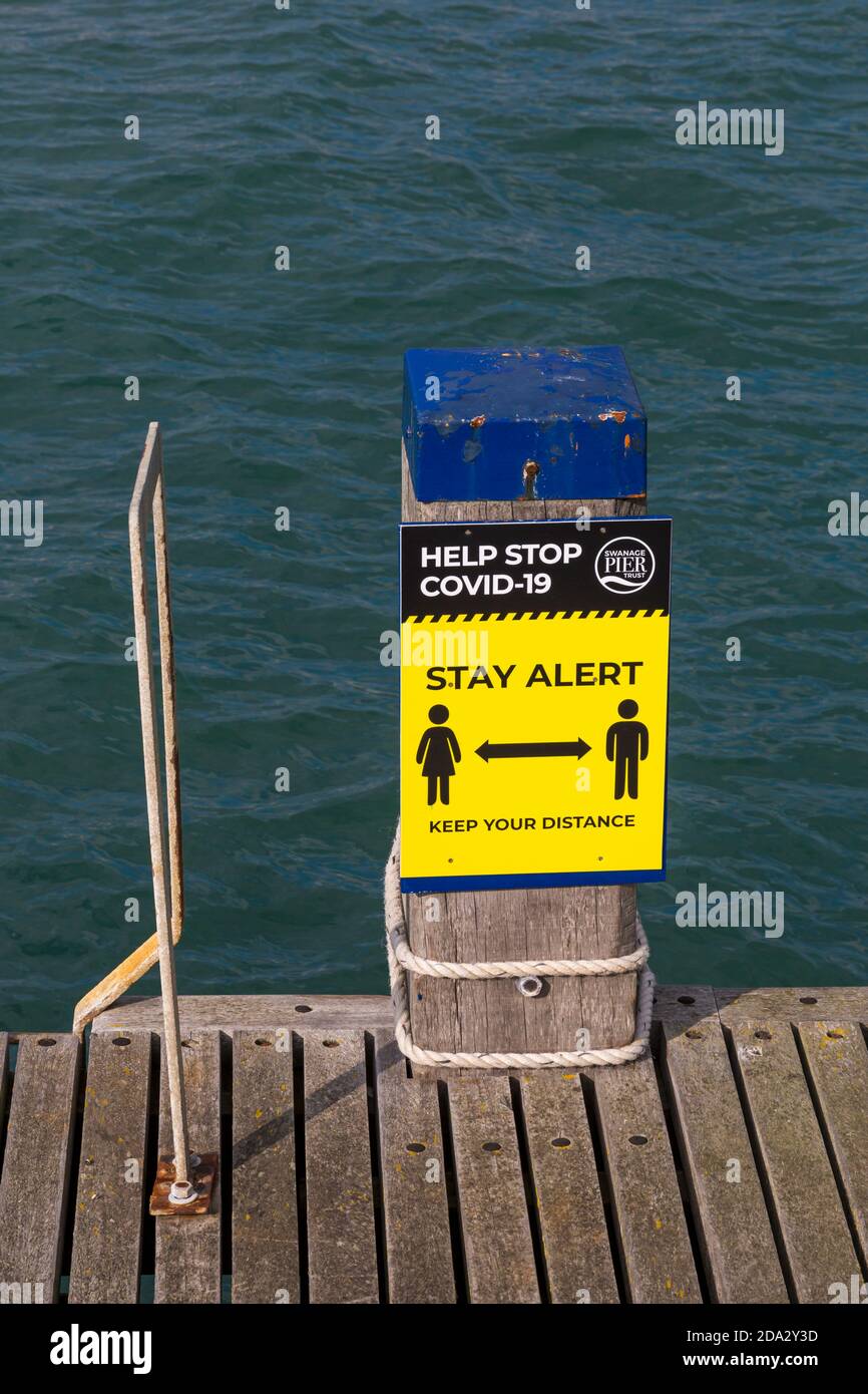 Aidez STOP Covid-19 Restez alerte Gardez votre signe de distance à côté du ponton sur Swanage Pier à Swanage, Dorset UK en octobre Banque D'Images