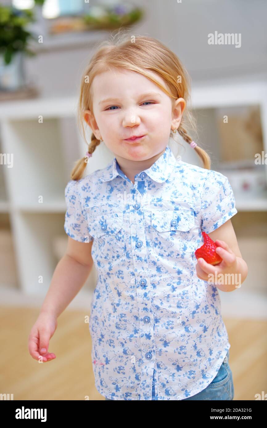 Enfant avec fraise a sa bouche pleine dans la cuisine à la maison Banque D'Images