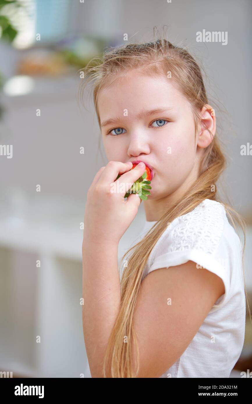 Enfant blond qui mange de la fraise à la maison dans la cuisine Banque D'Images