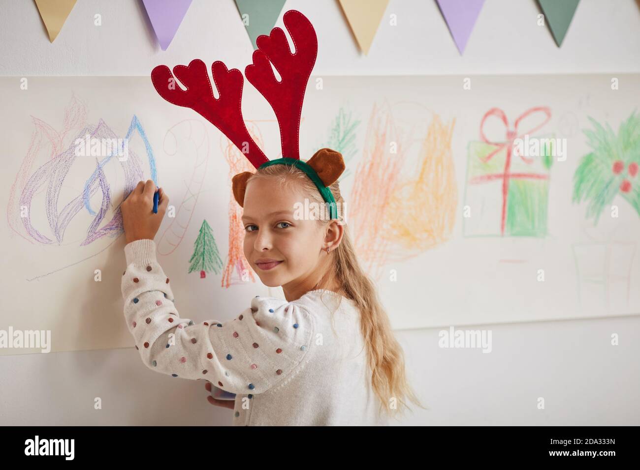 Portrait de fille blonde souriante portant des bois dessinant des images de Noël sur le mur pendant la classe d'art, espace de copie Banque D'Images