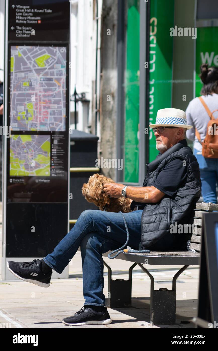 WINCHESTE, ROYAUME-UNI - 16 juillet 2020: Homme plus âgé en sport, assis sur un banc avec un chien sur une laisse près de la carte Winchester, Sunny sumer day chi Banque D'Images