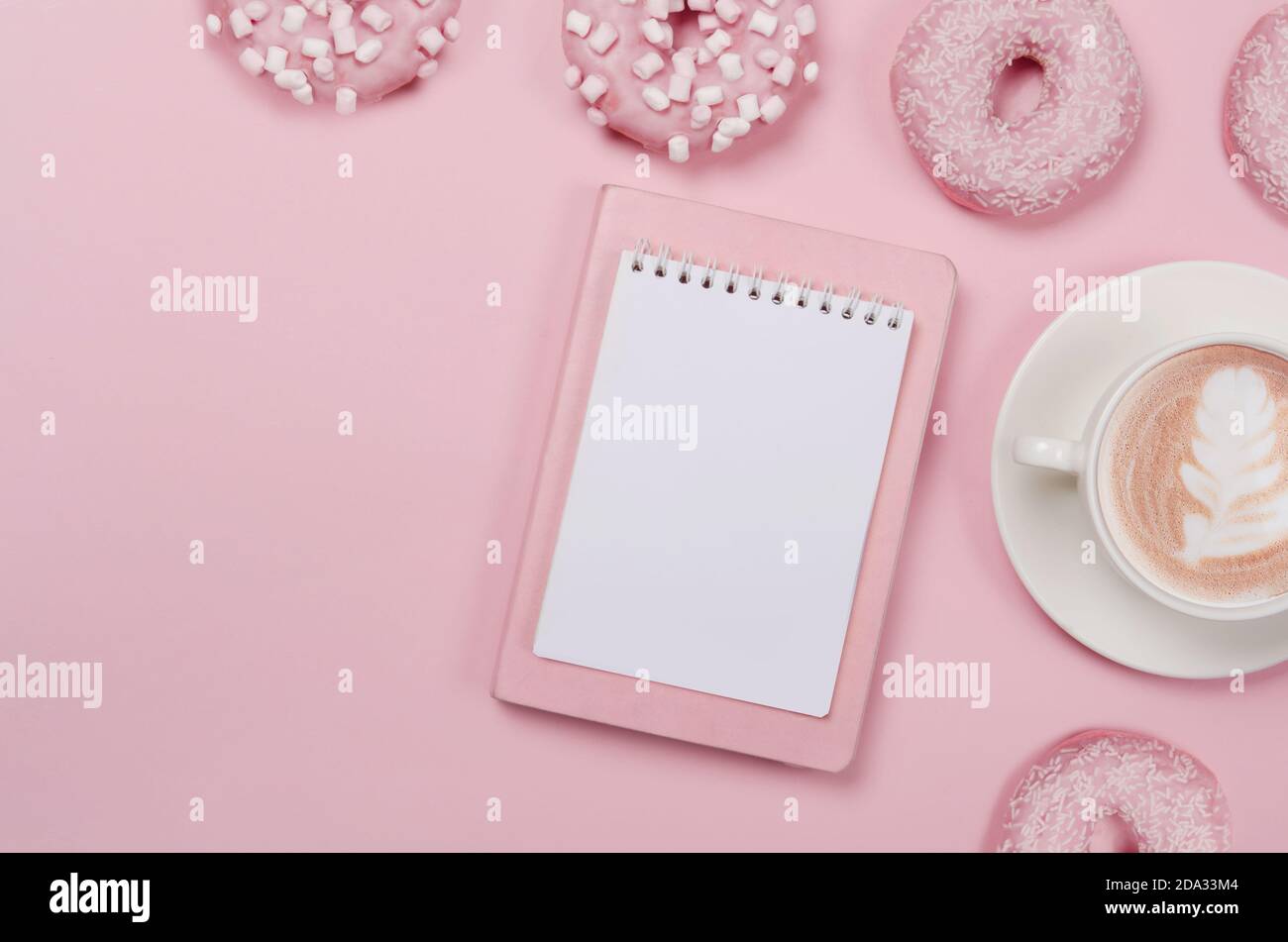 Bloc-notes liste de souhaits pour les plans futurs. composition de la pose à plat avec beignets, bloc-notes et tasse de café sur fond rose Banque D'Images