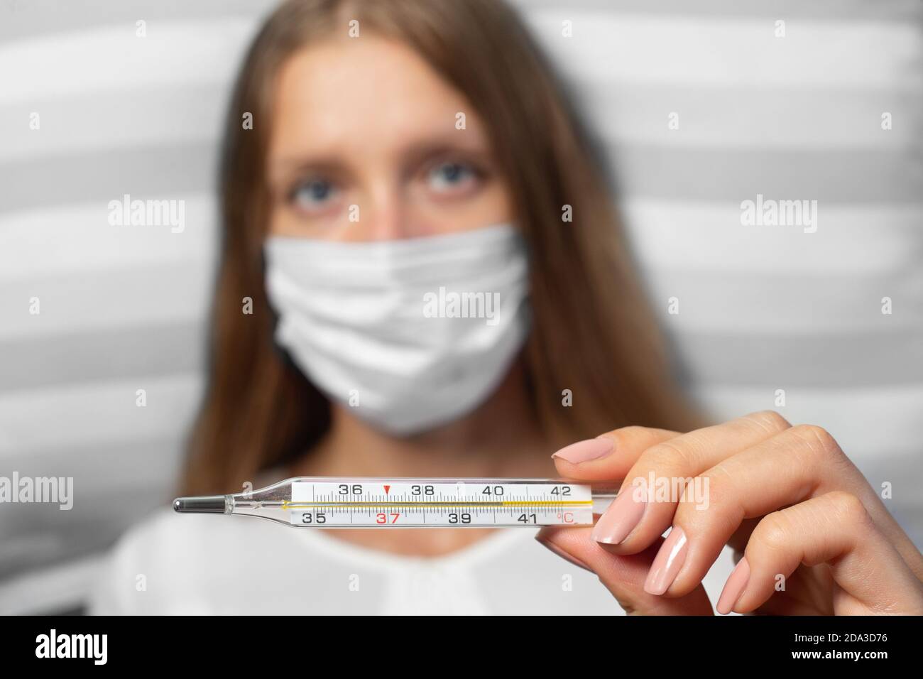 La jeune femme porte un masque médical et un thermomètre. Isolé sur fond blanc. Concept des épidémies de pneumonie, des épidémies de coronavirus a Banque D'Images