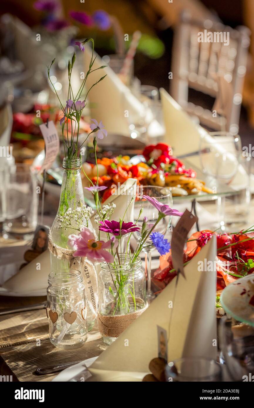 Fleurs dans des pots de confiture en verre sur une table lors d'une réception de mariage. Banque D'Images