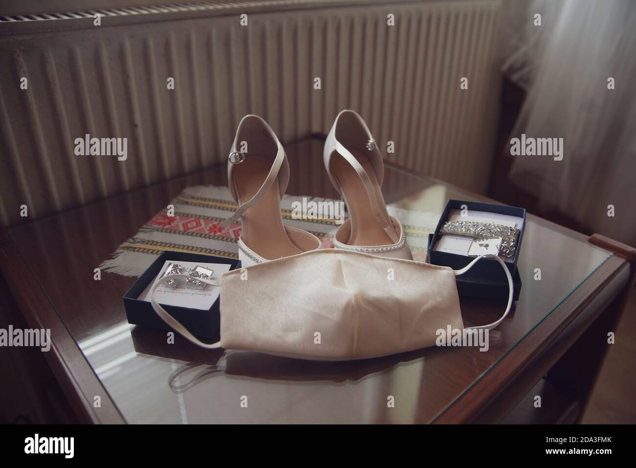 Une paire de chaussures blanches pour une mariée couverte de masque, à côté de ses bijoux sur une table basse en bois Banque D'Images