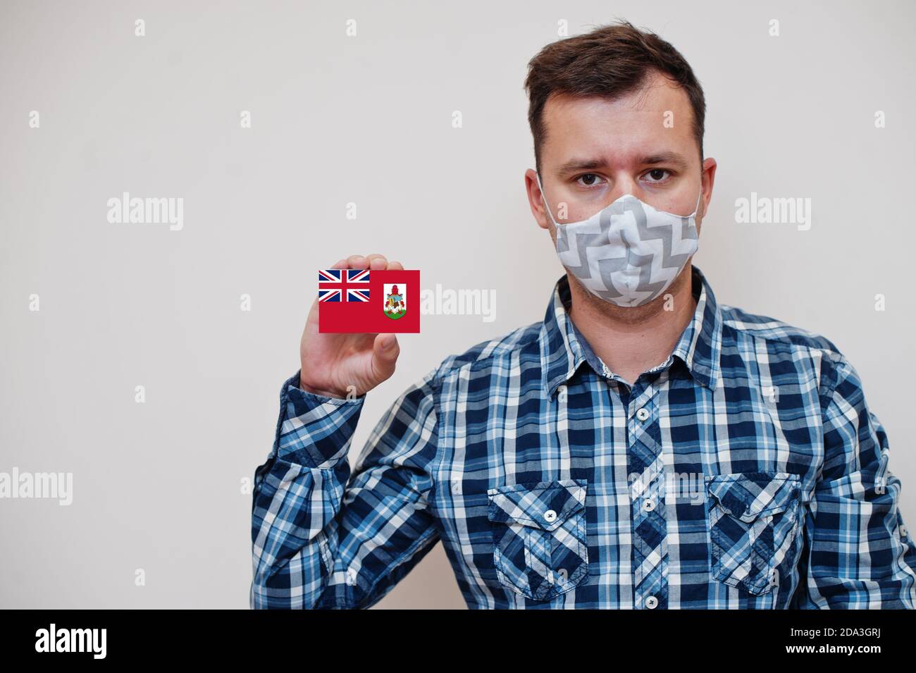 Homme en chemise à carreaux affiche carte drapeau Bermudes en main, porter un masque de protection isolé sur fond blanc. Concept du coronavirus des pays américains. Banque D'Images