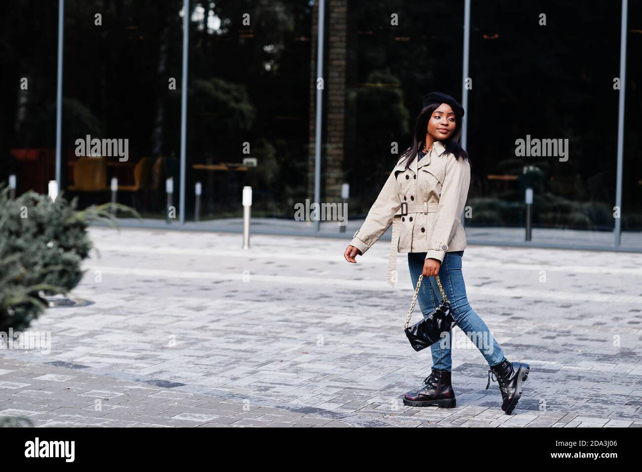 La femme afro-américaine à la mode porte un béret et un manteau avec sac à main posé à l'extérieur. Banque D'Images