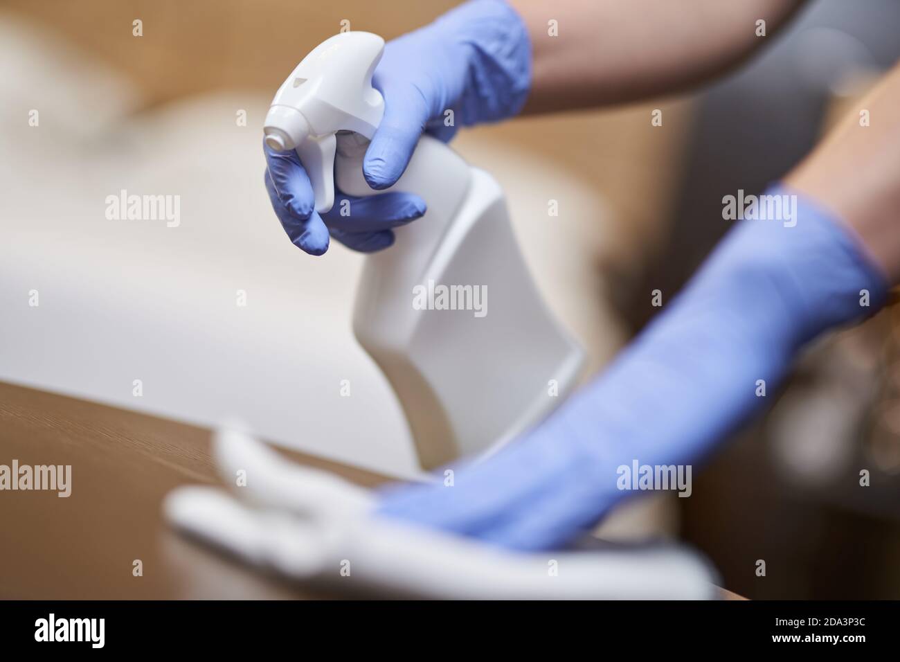 Gros plan de de housemaid dans des gants pulvérisant du désinfectant sur les meubles pendant le nettoyage de la chambre d'hôtel. Concept de ménage et d'hygiène Banque D'Images