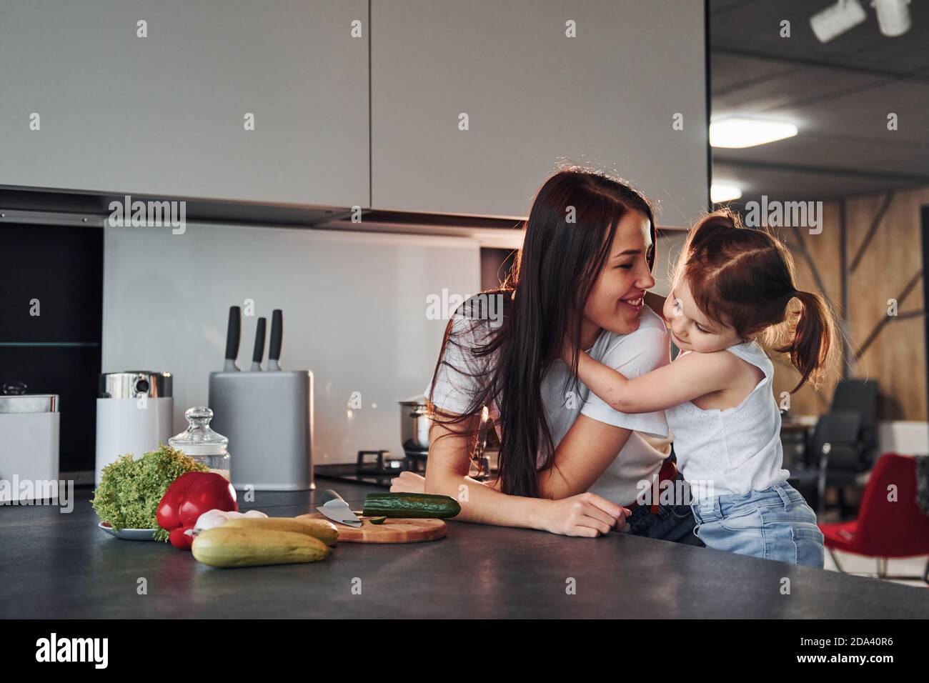 Mère avec sa petite fille qui coupe des légumes à l'intérieur dans la cuisine Banque D'Images