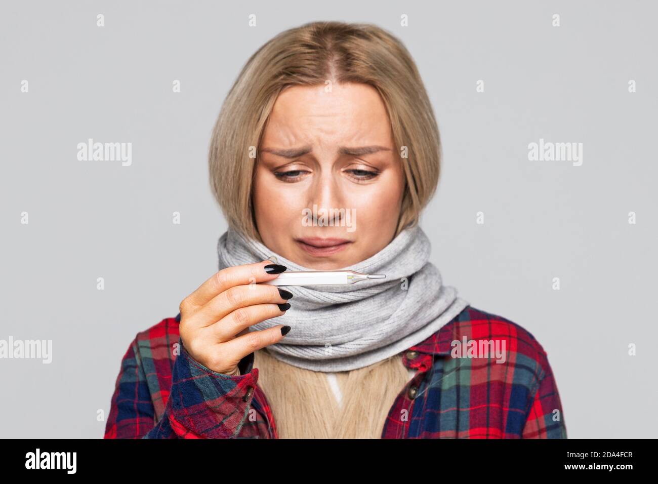 Une femme malsaine a attrapé le froid et regarde le thermomètre. Une femme bouleversée dans un foulard, une chemise à carreaux se sent mal. Froid, maladie. Banque D'Images