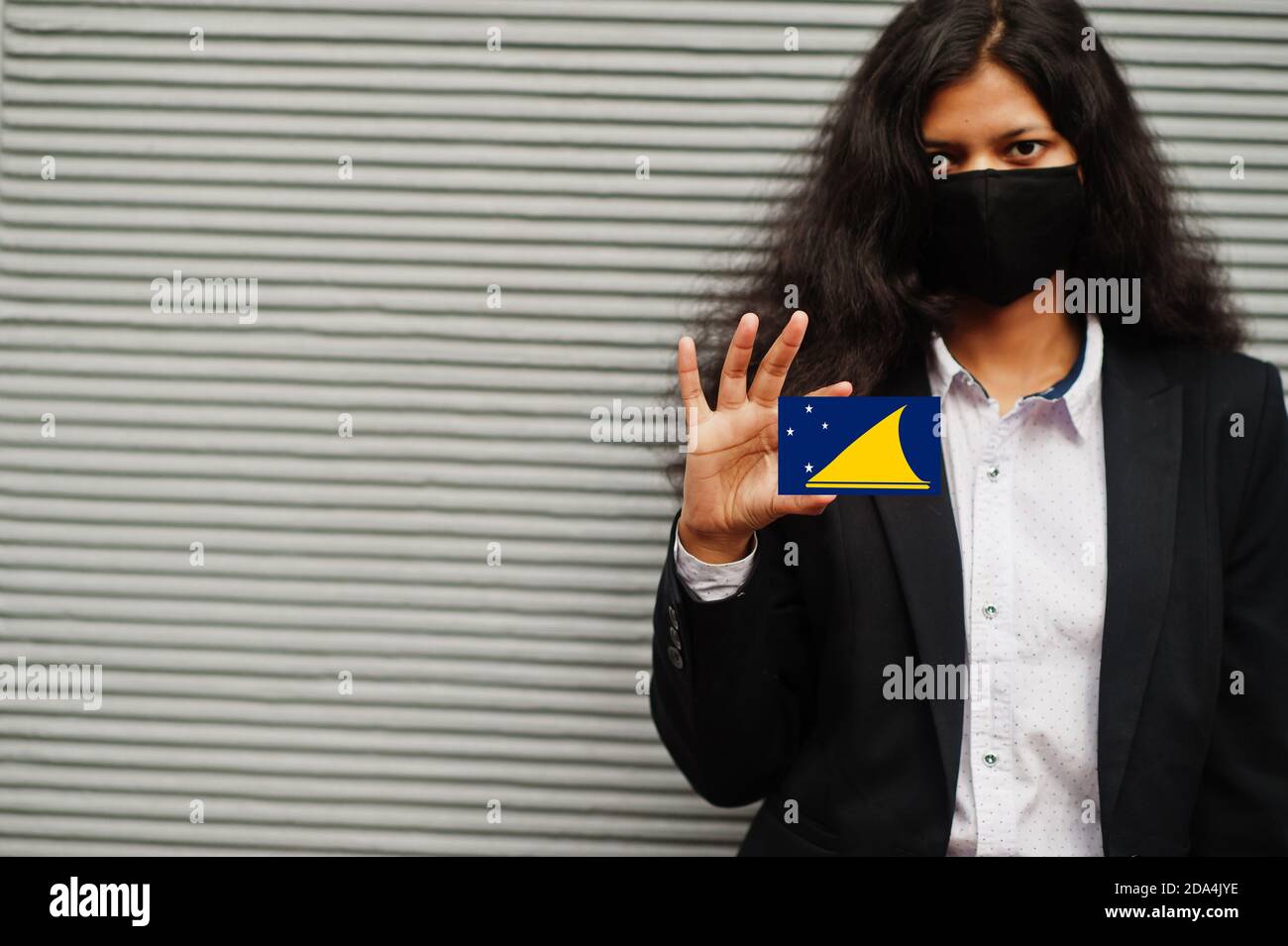 Femme asiatique en tenue officielle et noir masque de protection pour le visage tenir le drapeau Tokelau à la main sur fond gris. Coronavirus au concept de pays. Banque D'Images