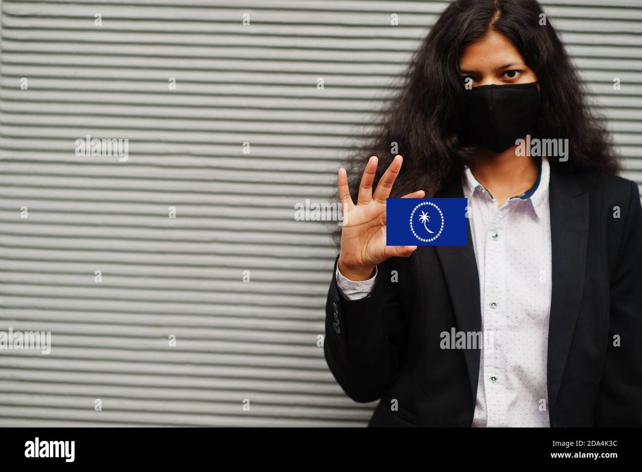 Femme asiatique en tenue officielle et noir masque de protection tenir le drapeau de l'État de Chuuk à la main sur fond gris. Coronavirus au concept de pays. Banque D'Images