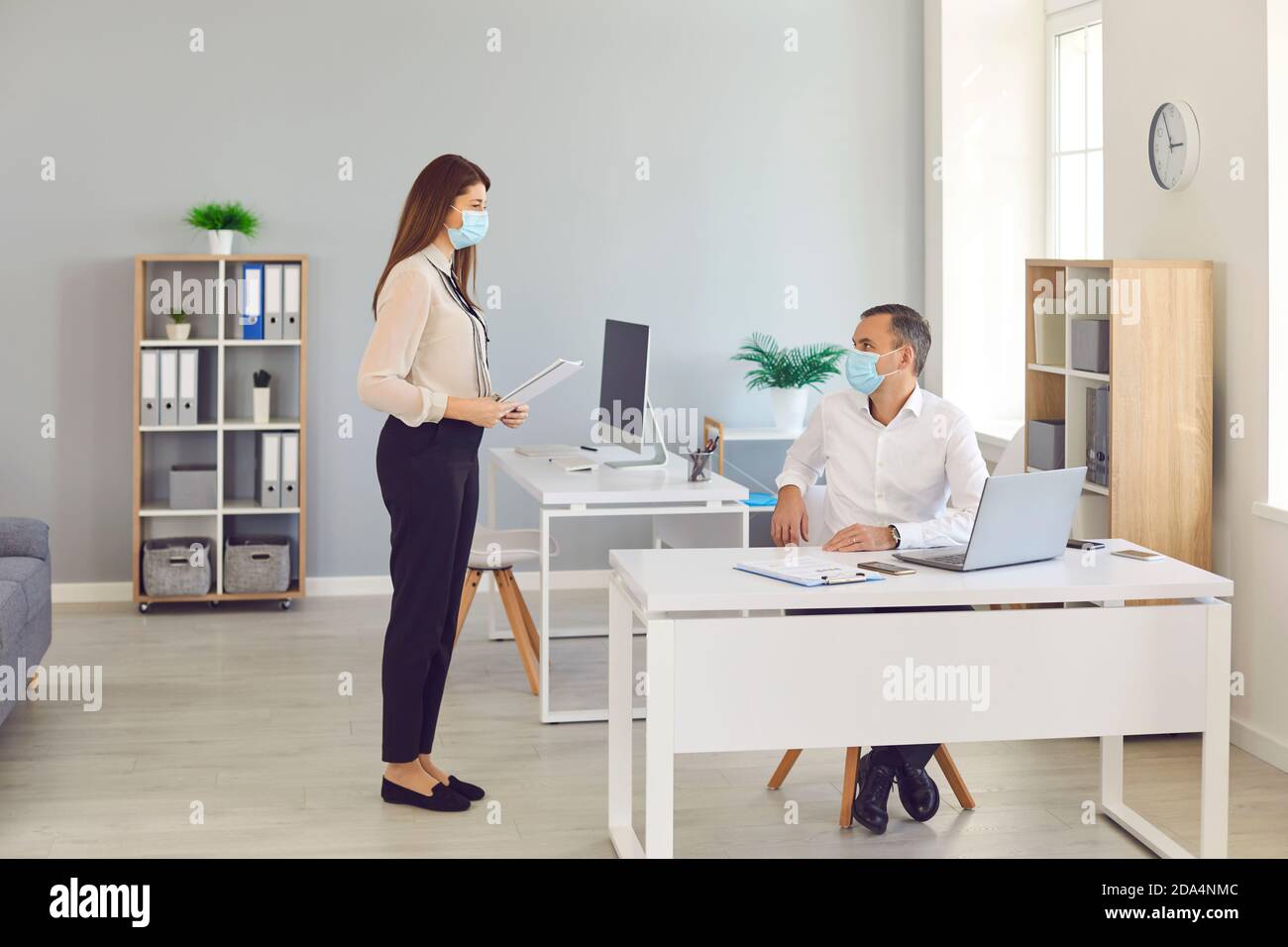 Les employés de bureau portant un masque de protection doivent respecter la distance de sécurité lorsqu'ils communiquent au bureau. Banque D'Images