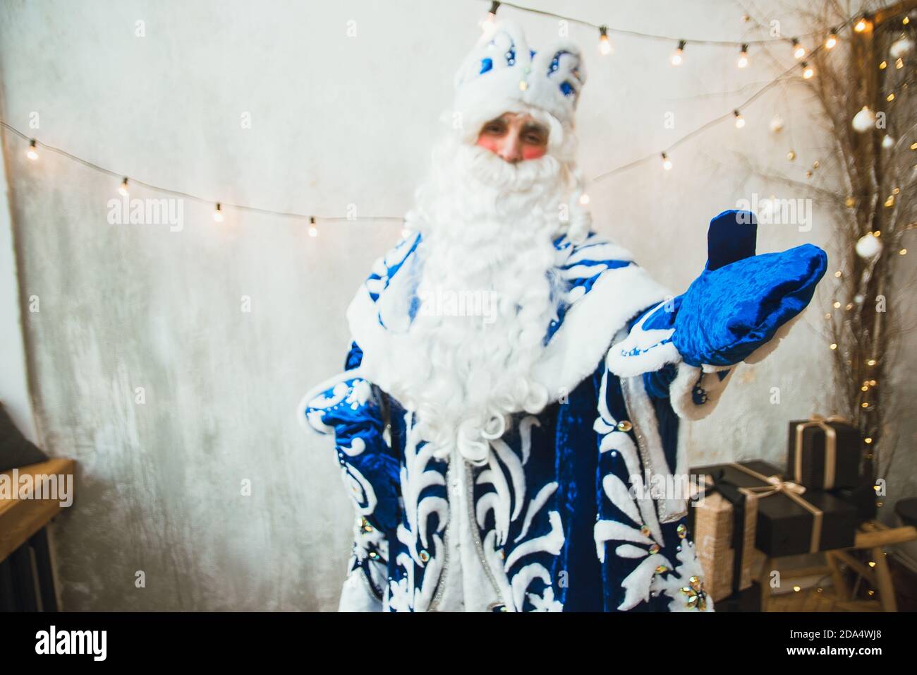 Le Père Noël en fourrure bleue se tient contre le Contexte d'une garland du nouvel an et points avec son main gantée à l'appareil photo Banque D'Images