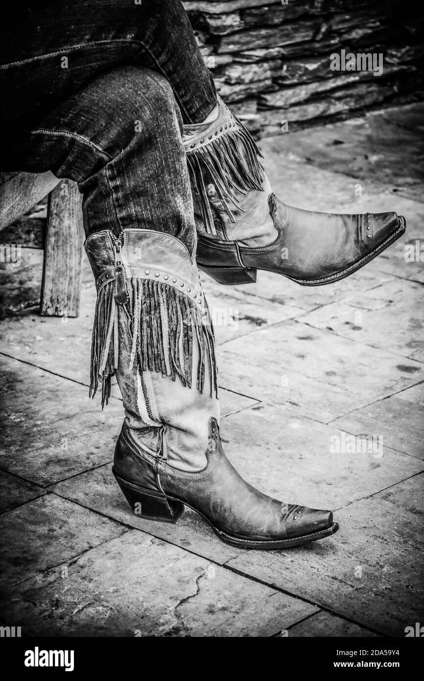 Gros plan sur les jambes de femme croisées dans un Jean à l'intérieur bottes de cowgirl à franges sur le trottoir en noir et blanc Le sud des États-Unis Banque D'Images