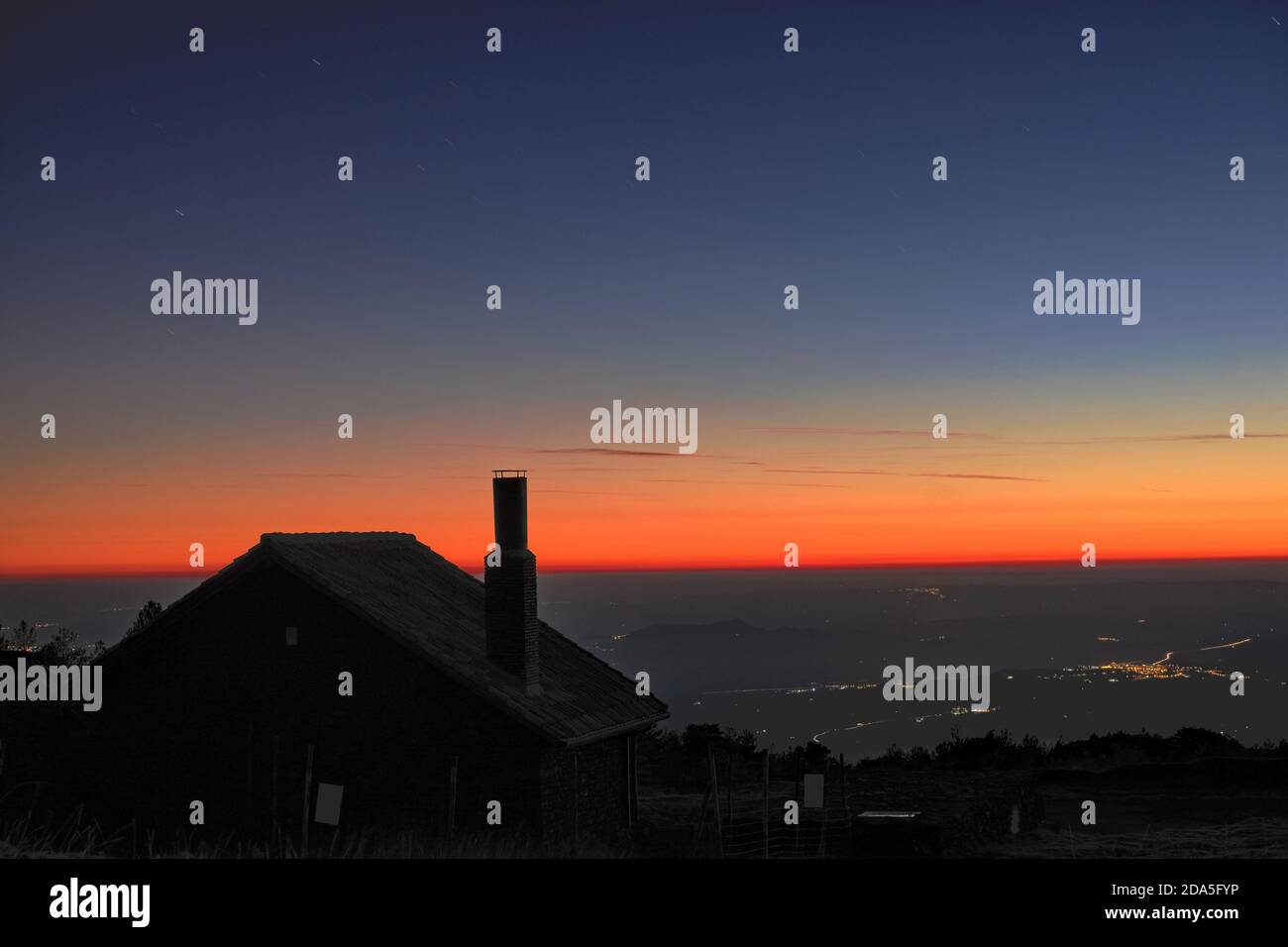 Silhouette de toit et cheminée de cabane de montagne contre le ciel crépuscule coloré et les lumières de nuit de la ville de l'Etna National Park, Sicile Banque D'Images