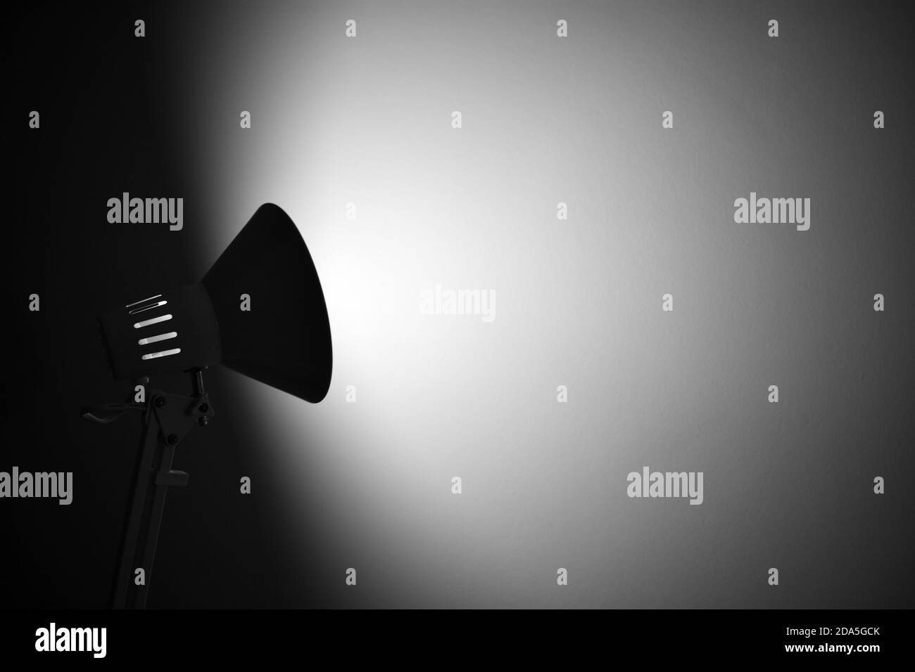Une silhouette d'une lampe de bureau réglable qui projette un spot sur un mur blanc Uni dans une pièce sombre. Espace de copie et grandes zones vierges. Banque D'Images
