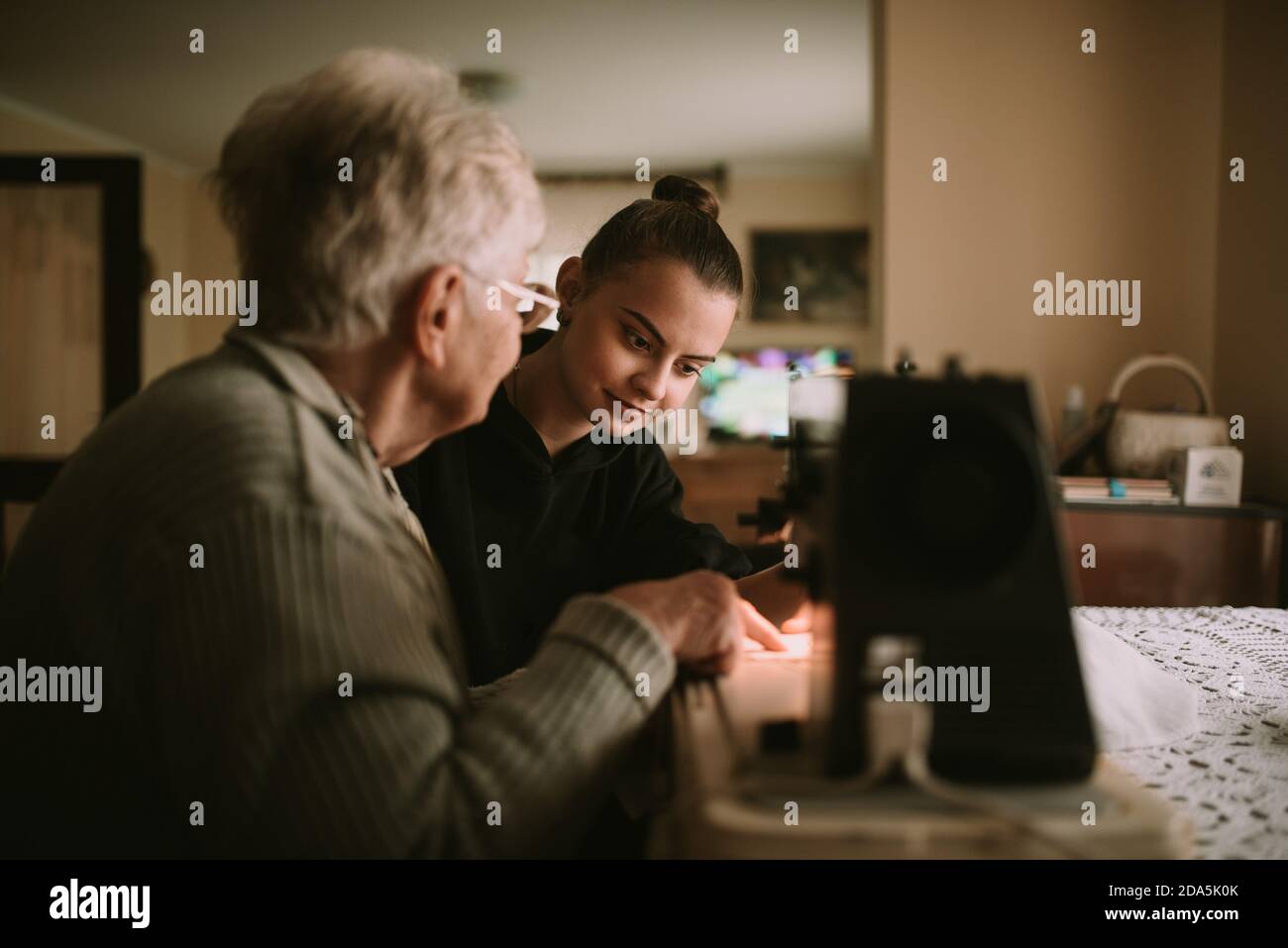 La petite-mère sucrée senior explique à sa belle petite-fille adolescente à coudre des vêtements sur une machine à coudre dans la maison de sa grand-mère Banque D'Images