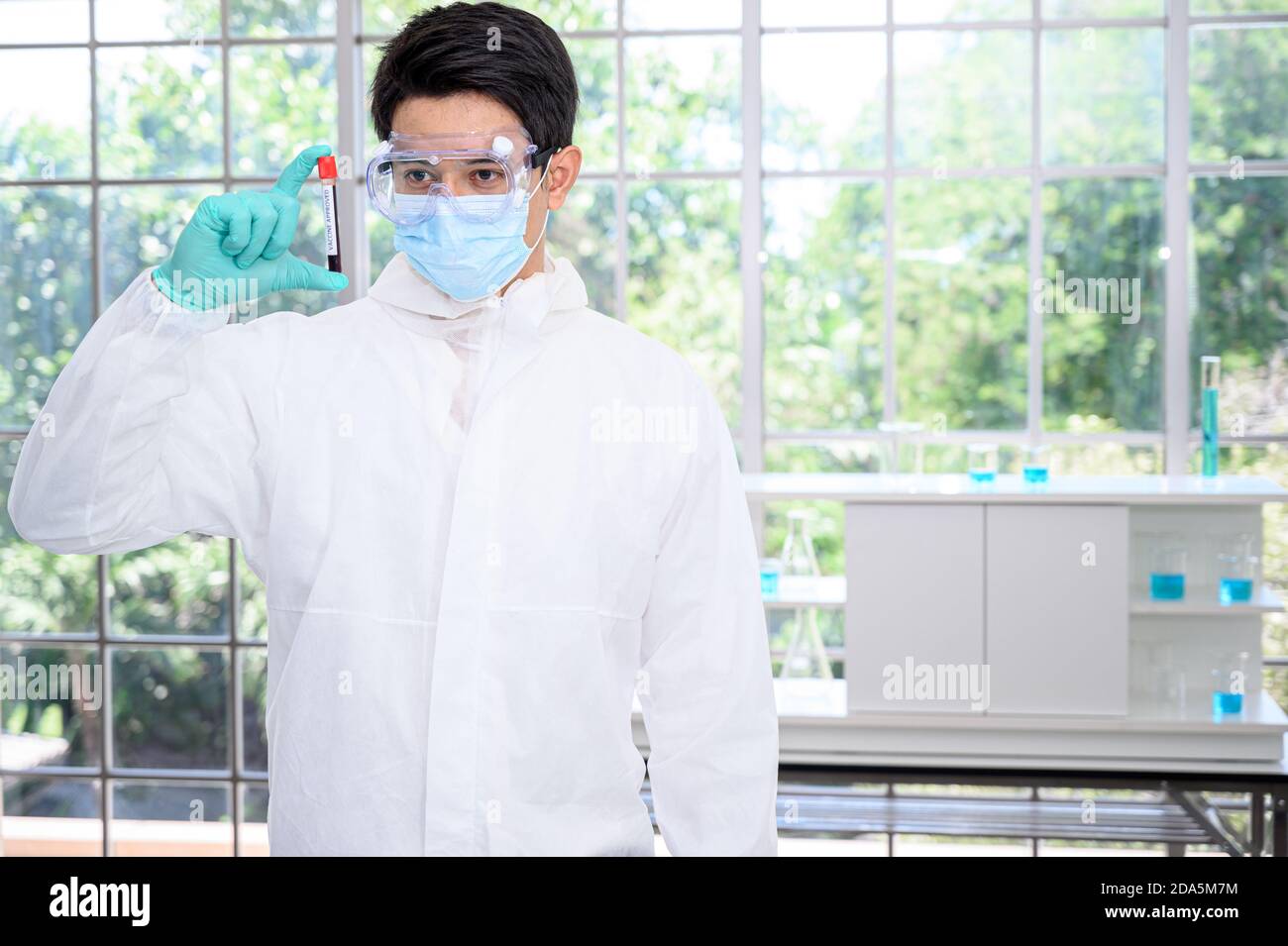 Un scientifique mâle portant une combinaison de protection tenant un vaccin et travaillant avec de nombreux équipements de laboratoire pour la recherche d'un vaccin en laboratoire. Spécifications du chercheur médical Banque D'Images