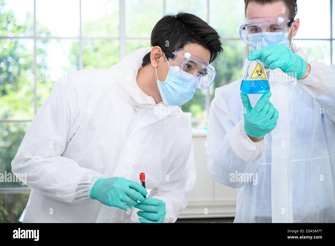 Couple de scientifiques mâles portant une combinaison de protection tenant le vaccin et travaillant avec de nombreux équipements de laboratoire pour la recherche de vaccins en laboratoire. Recherche médicale Banque D'Images