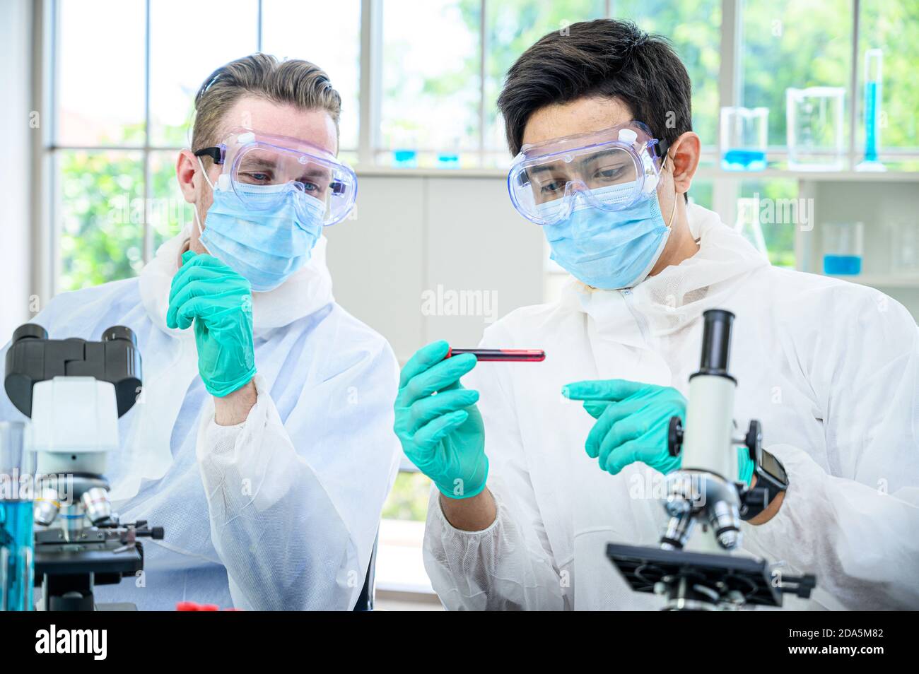 Couple de scientifiques mâles portant une combinaison de protection tenant le vaccin et travaillant avec de nombreux équipements de laboratoire pour la recherche de vaccins en laboratoire. Recherche médicale Banque D'Images