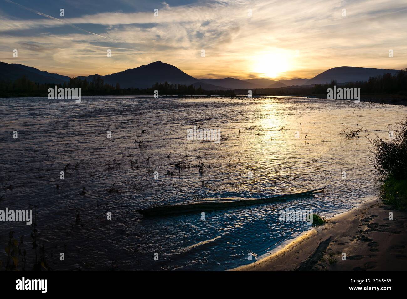 Réflexions du soleil sur les eaux ondulantes de la rivière Piave au coucher du soleil. En arrière-plan, le soleil et le profil des montagnes dans la brume. Sa Banque D'Images