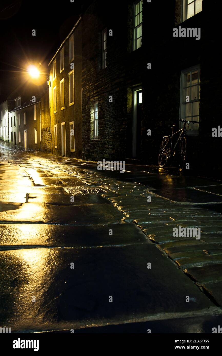 Rue sombre et spectaculaire la nuit avec vélo et réflexions sur les dalles de pierre humides Banque D'Images