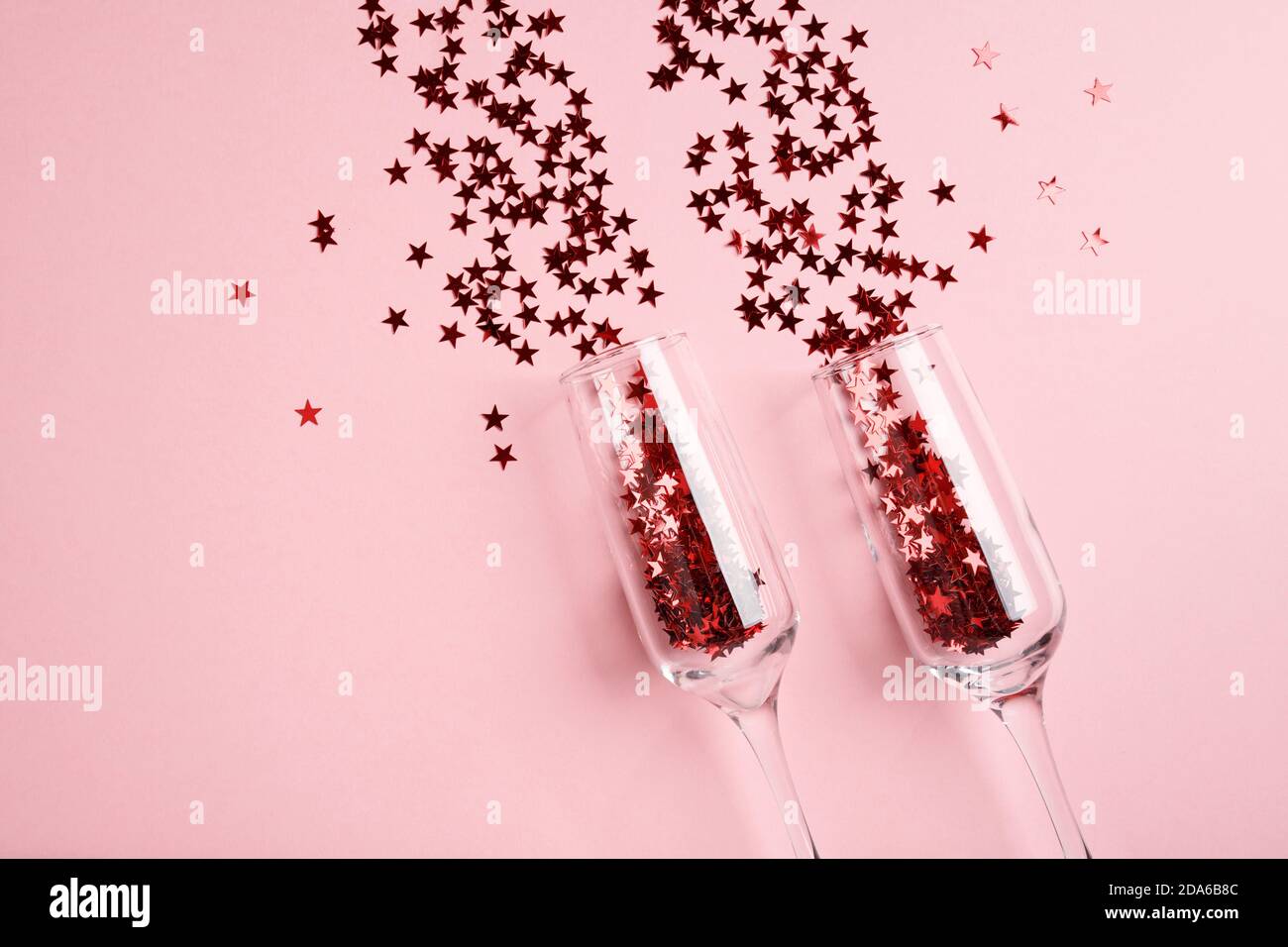 Coupe de champagne avec confetti rouges sur fond rose. Banque D'Images
