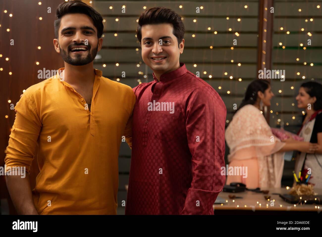 DEUX COLLÈGUES MASCULINS REGARDANT LA CAMÉRA ET POSANT AVEC UNE FEMME SES COLLÈGUES SE FONT DES CADEAUX EN ARRIÈRE-PLAN Banque D'Images