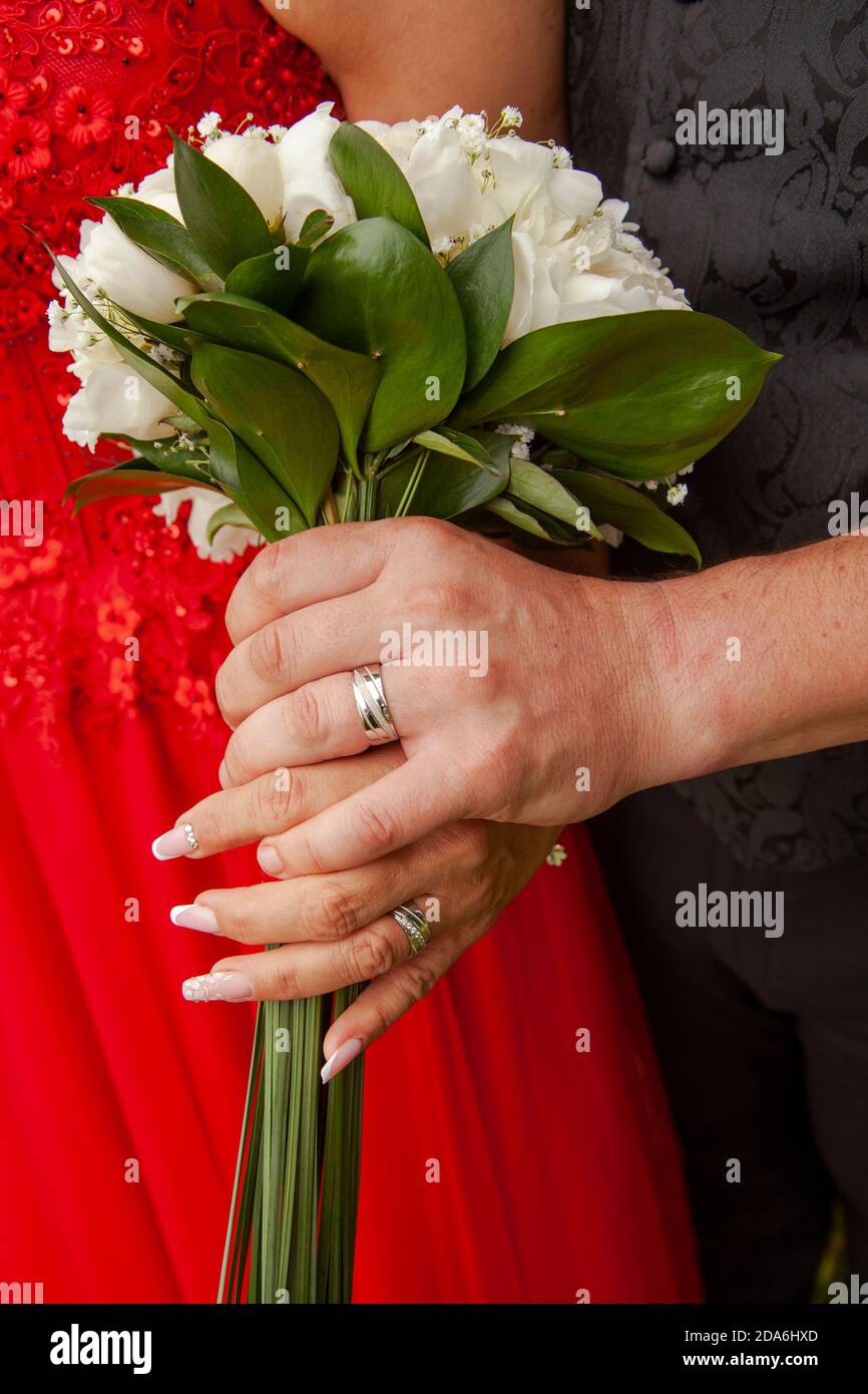 Un gros plan d'un nouveau-lyweds mains tenant un bouquet avec des anneaux de mariage sur eux Banque D'Images
