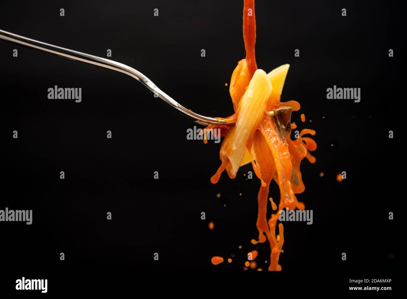 un filet de sauce tomate tombe sur une fourchette avec les pâtes créent de nombreuses éclaboussures sur un fond noir Banque D'Images