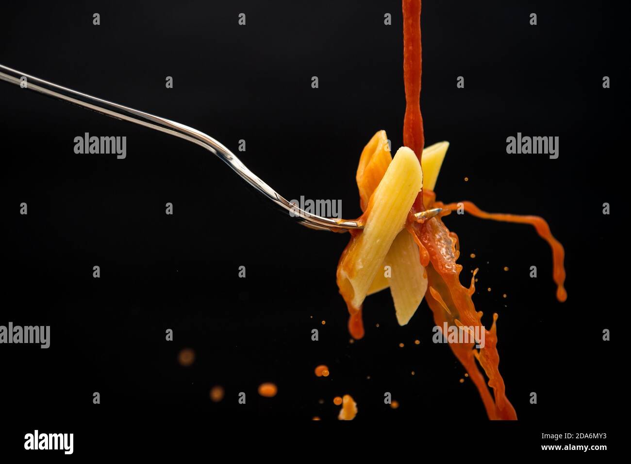 un filet de sauce tomate tombe sur une fourchette avec les pâtes créent de nombreuses éclaboussures sur un fond noir Banque D'Images