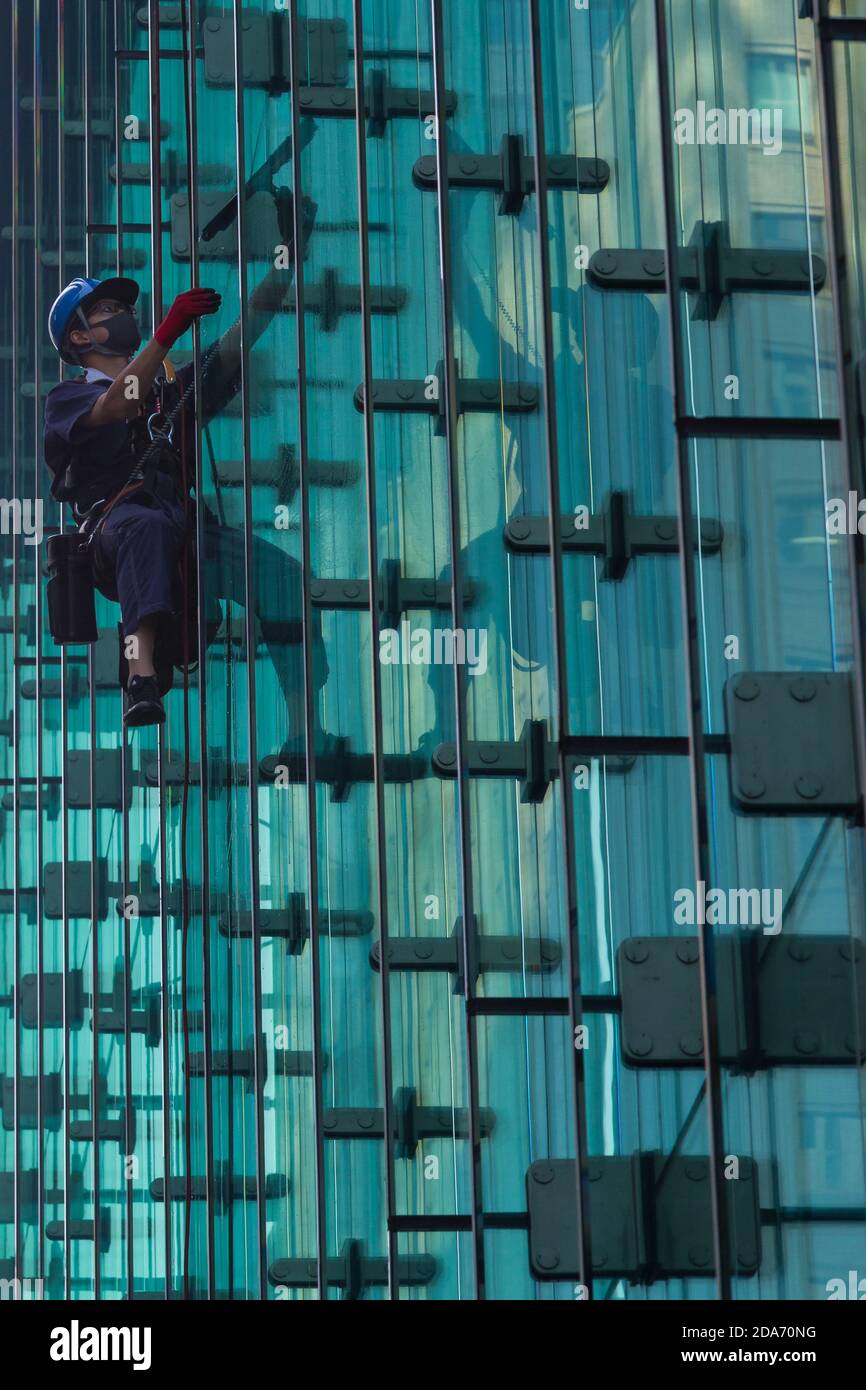 Un nettoyeur de fenêtres utilisant des cordes de descente pour nettoyer les fenêtres d'un immeuble de bureaux en verre à Otemachi, Tokyo, Japon. Banque D'Images