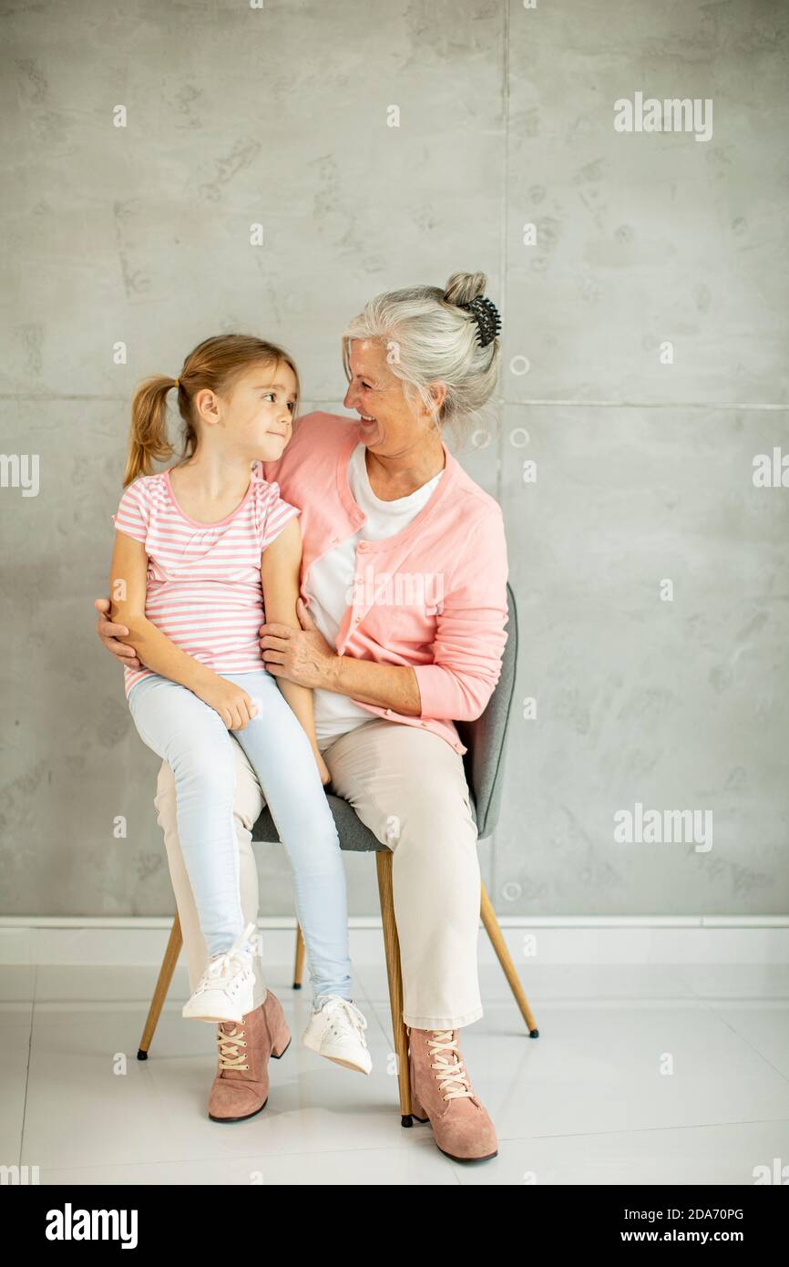 Petite fille avec sa grand-mère assise sur la chaise près du mur gris Banque D'Images