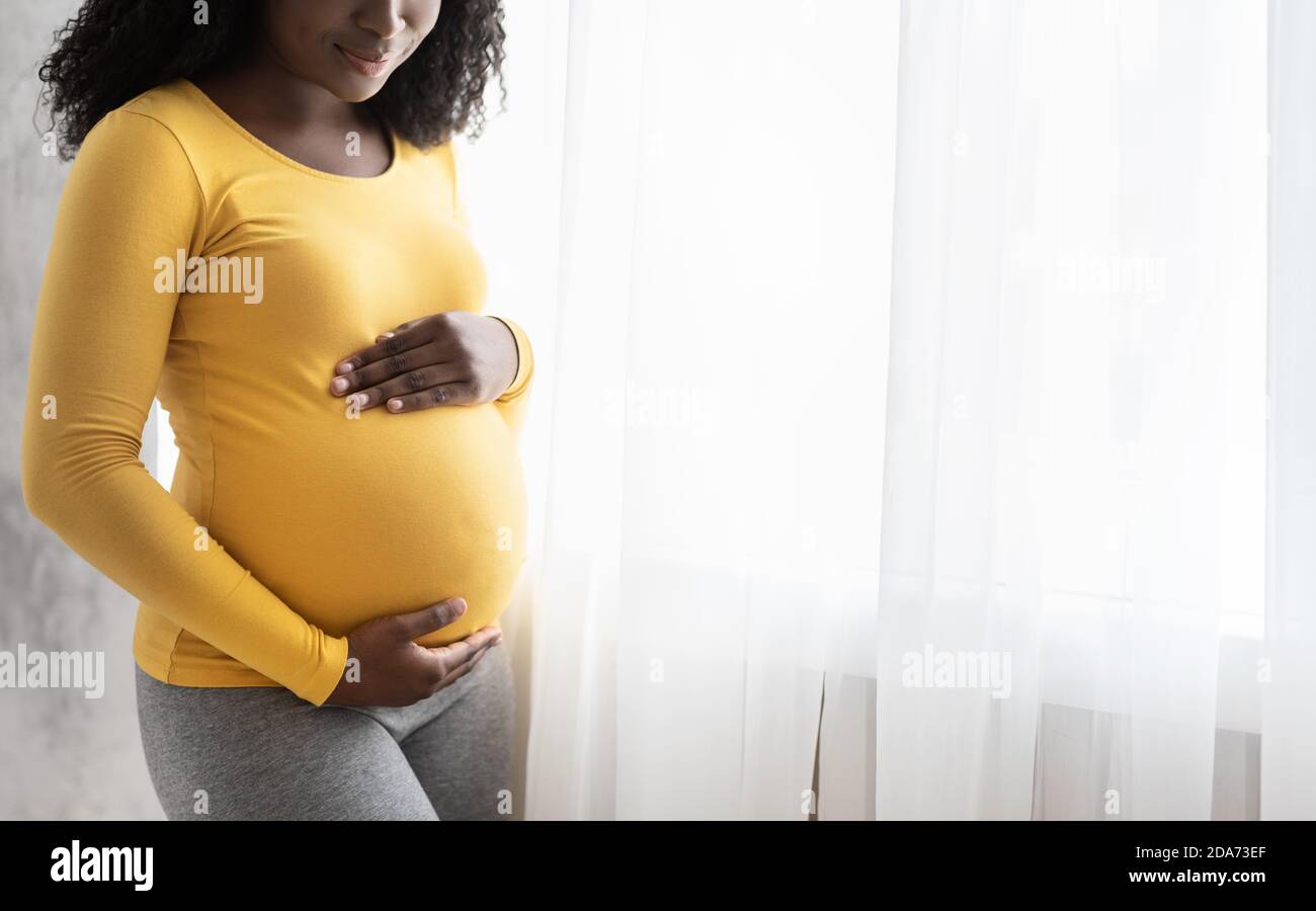 Écourté de femme enceinte noire debout près de la fenêtre Banque D'Images