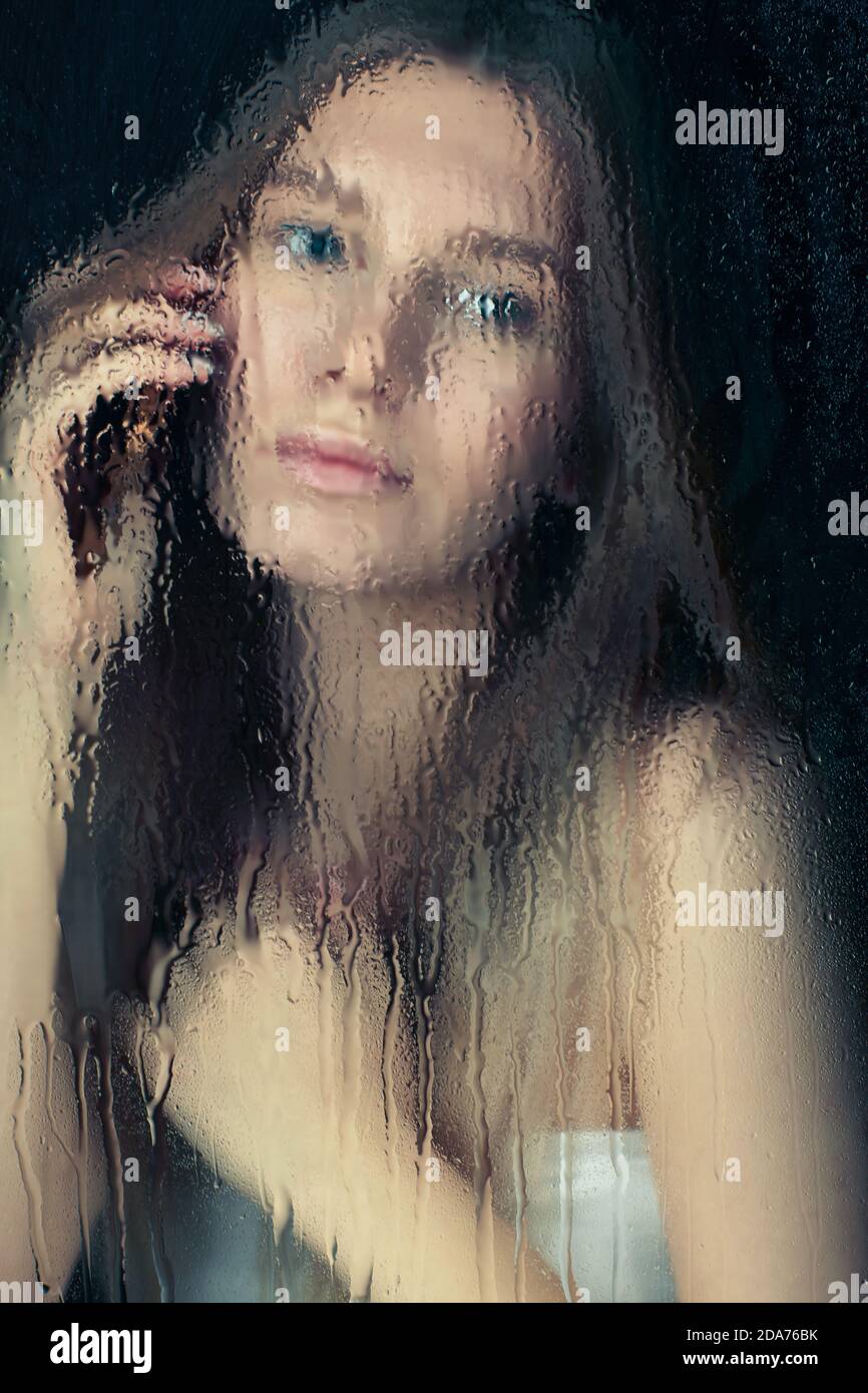 Portrait d'une jeune femme blonde avec les mains du téléphone. Femelle derrière la vitre avec gouttes de pluie. Concept de verrouillage d'auto-isolation. Banque D'Images