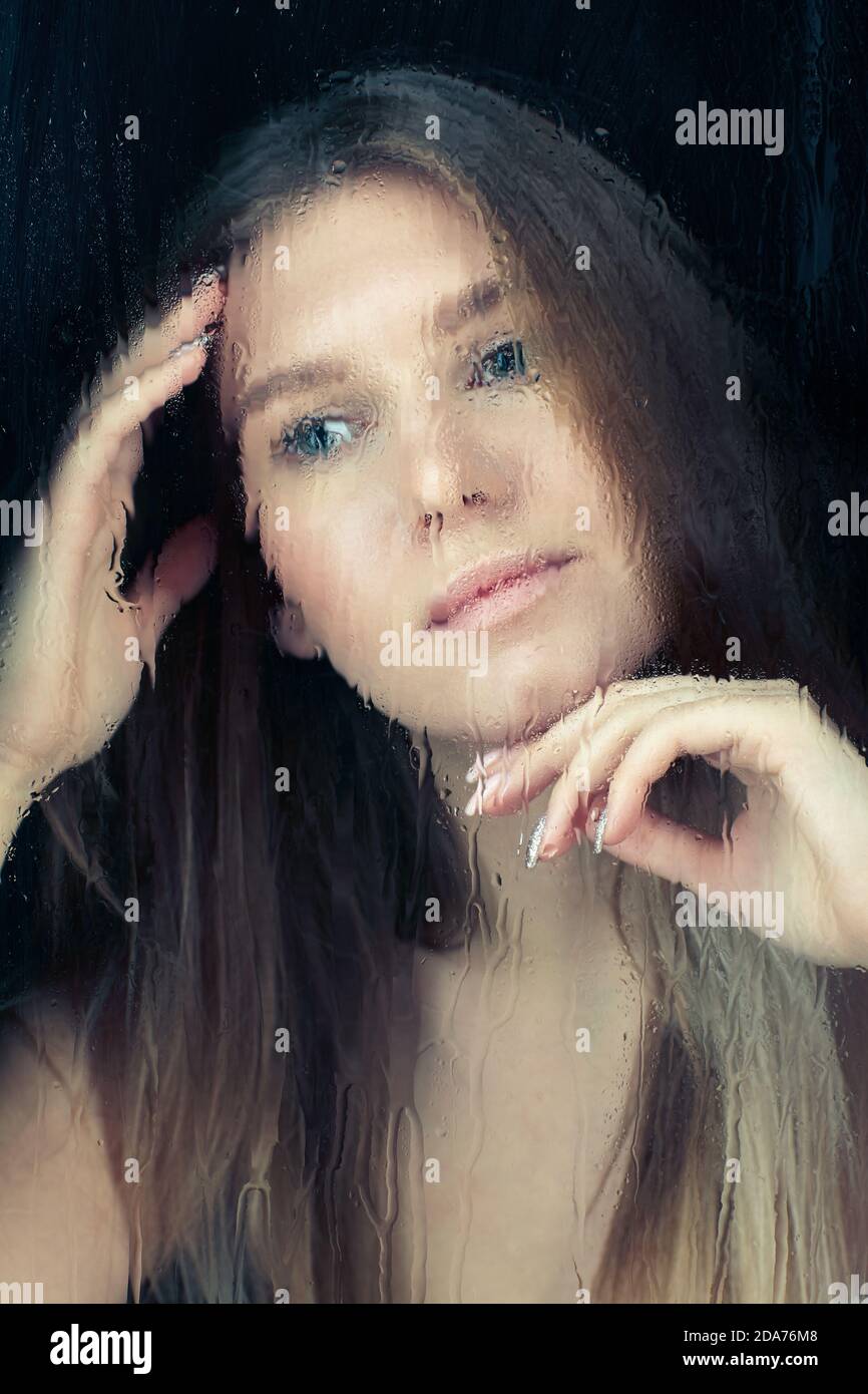 Portrait de jeune femme blonde derrière la vitre avec gouttes de pluie. Concept de verrouillage d'auto-isolation. Banque D'Images