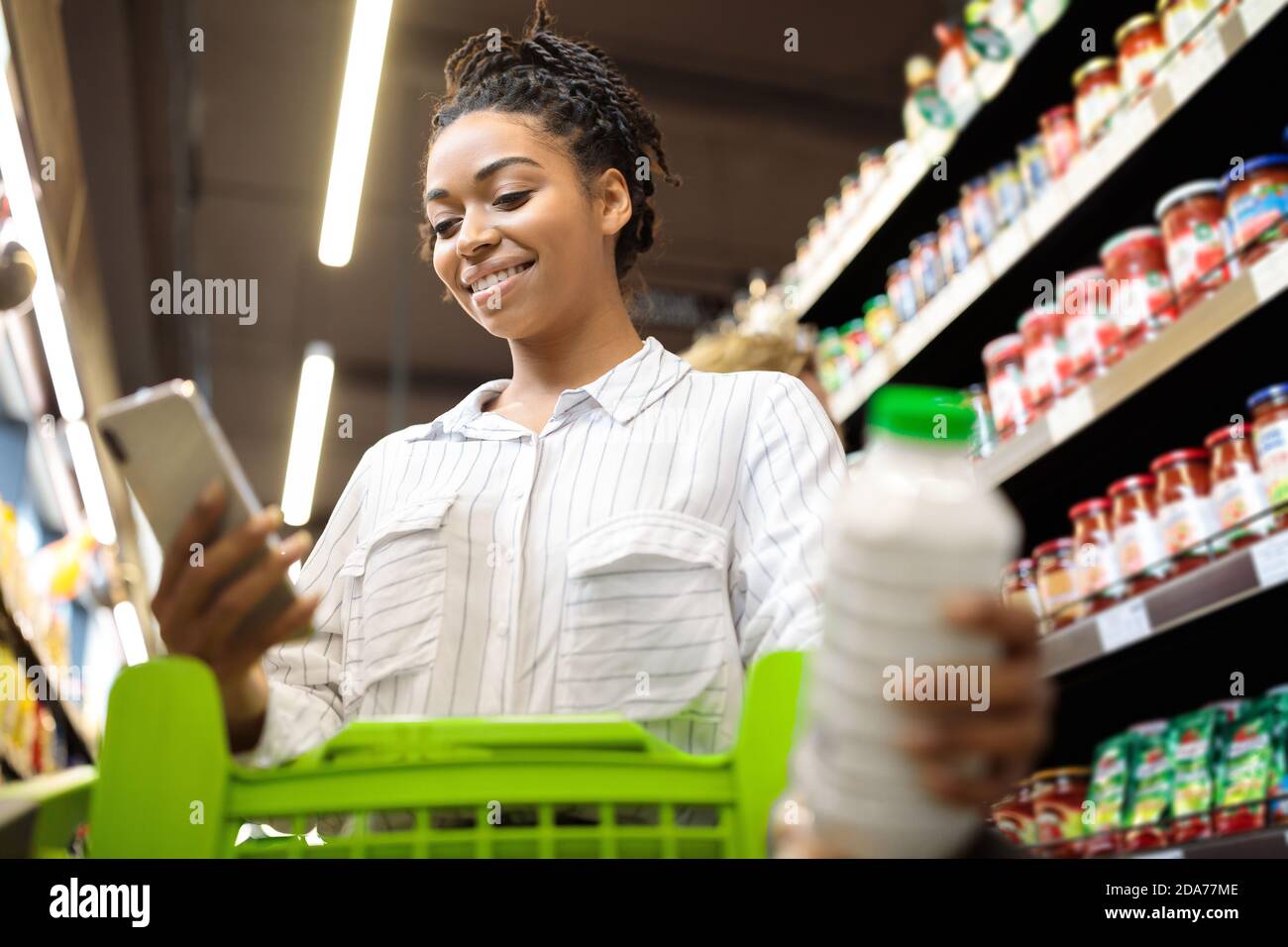 Lady utilisant le téléphone cellulaire avec l'application de shopping d'épicerie dans le supermarché Banque D'Images