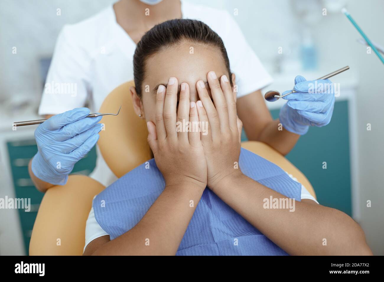 Fille effrayée couvre le visage avec les mains et ne permet pas médecin pour traiter la bouche avec des instruments médicaux dans les mains Banque D'Images