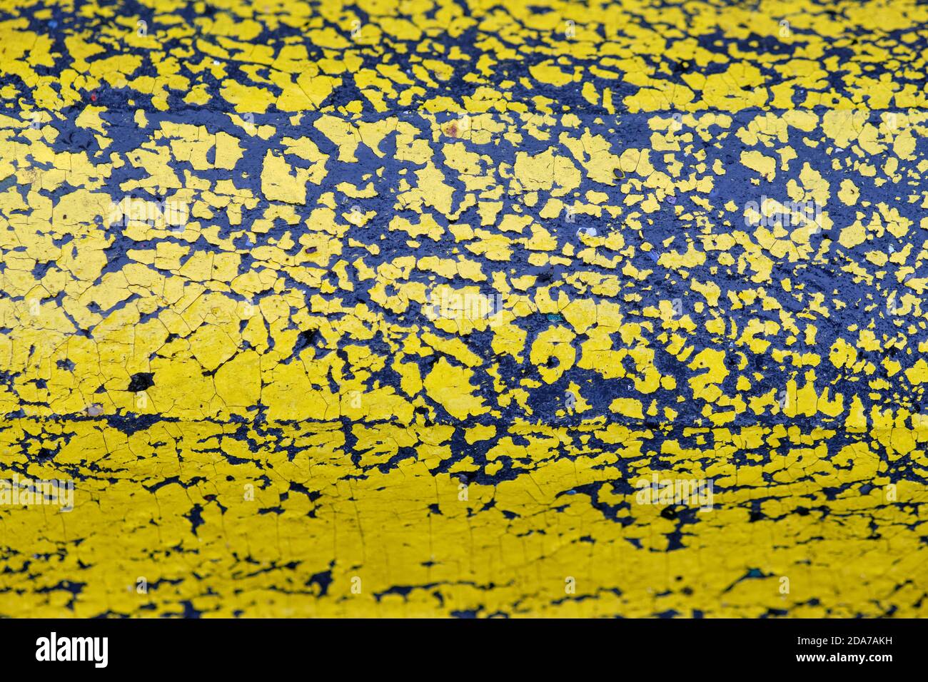 Arrière-plan avec gros plan de peinture jaune qui s'écaille d'une partie en plastique noir humide d'une limite de route. Vu en Allemagne en octobre. Banque D'Images
