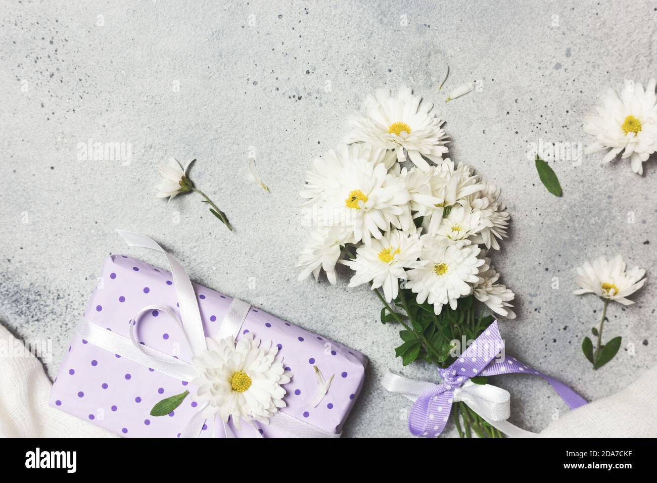 Bouquet de fleurs blanches et cadeau sur fond de béton gris, vue du dessus. Journée des femmes, anniversaire, jour de la Saint-Valentin ou arrière-plan de la fête des mères. Banque D'Images