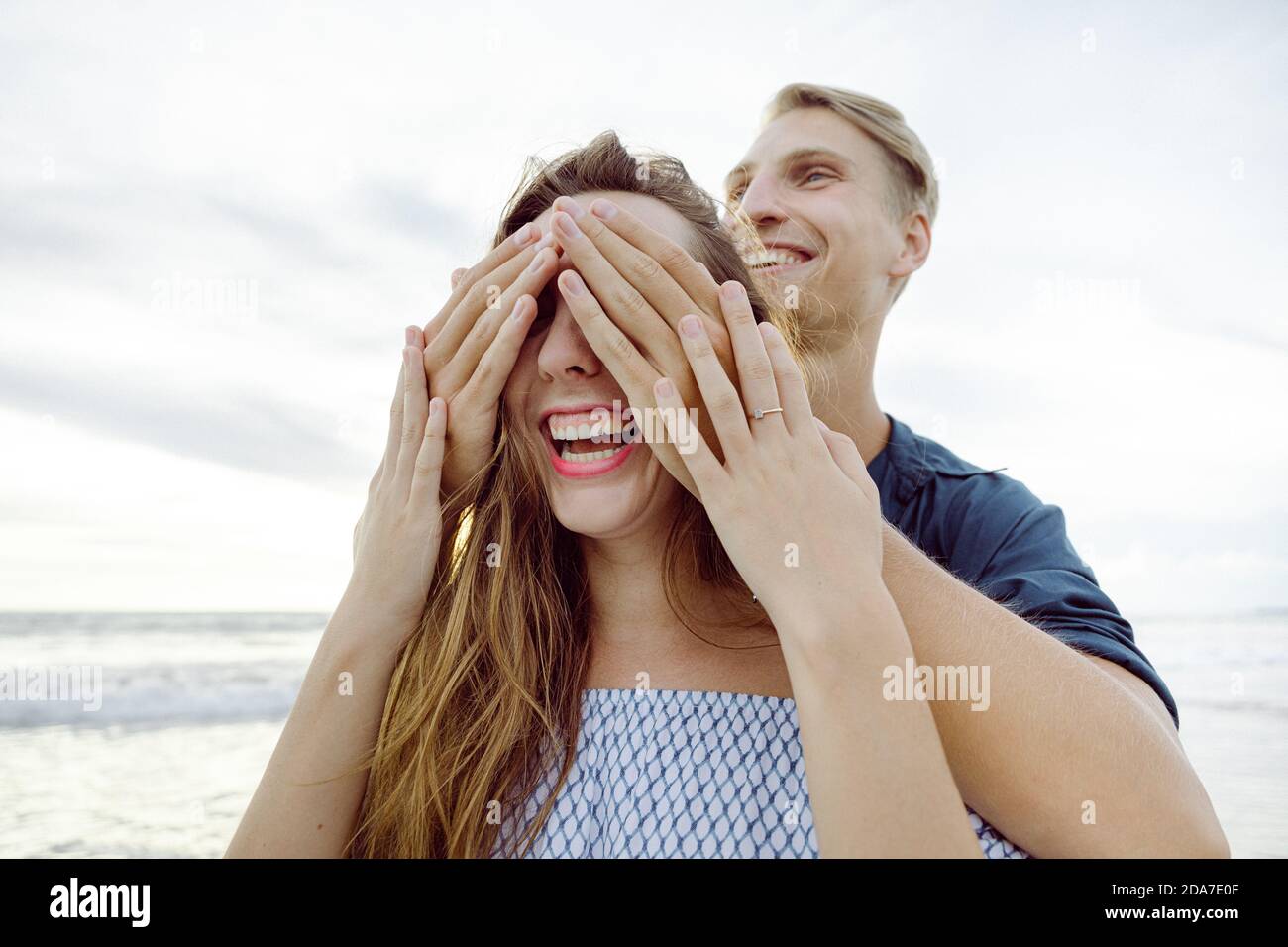 Homme couvrant les yeux de sa petite amie, rire ludique sur la plage Banque D'Images