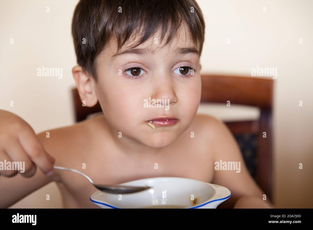 Le petit garçon mange avec une cuillère dans une assiette Banque D'Images