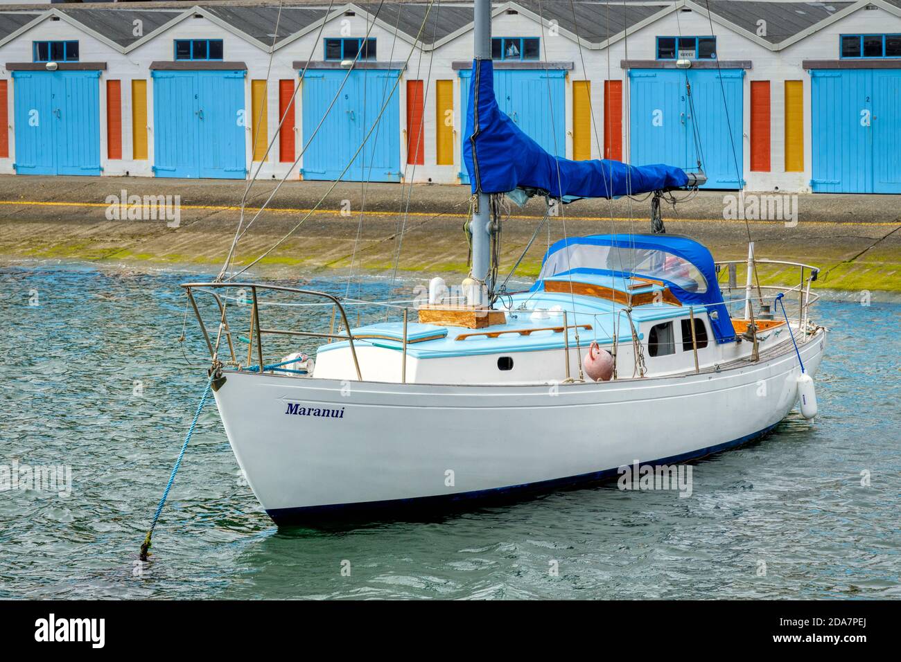 Bateau à voile Maranui ancré dans la baie orientale, Welling, Nouvelle-Zélande. Couleurs assorties aux hangars à bateaux historiques en arrière-plan. Port de plaisance de Clyde Quay. Banque D'Images