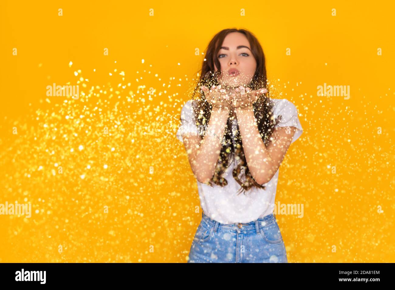 belle femme brunette soufflant de paillettes sur fond jaune Banque D'Images