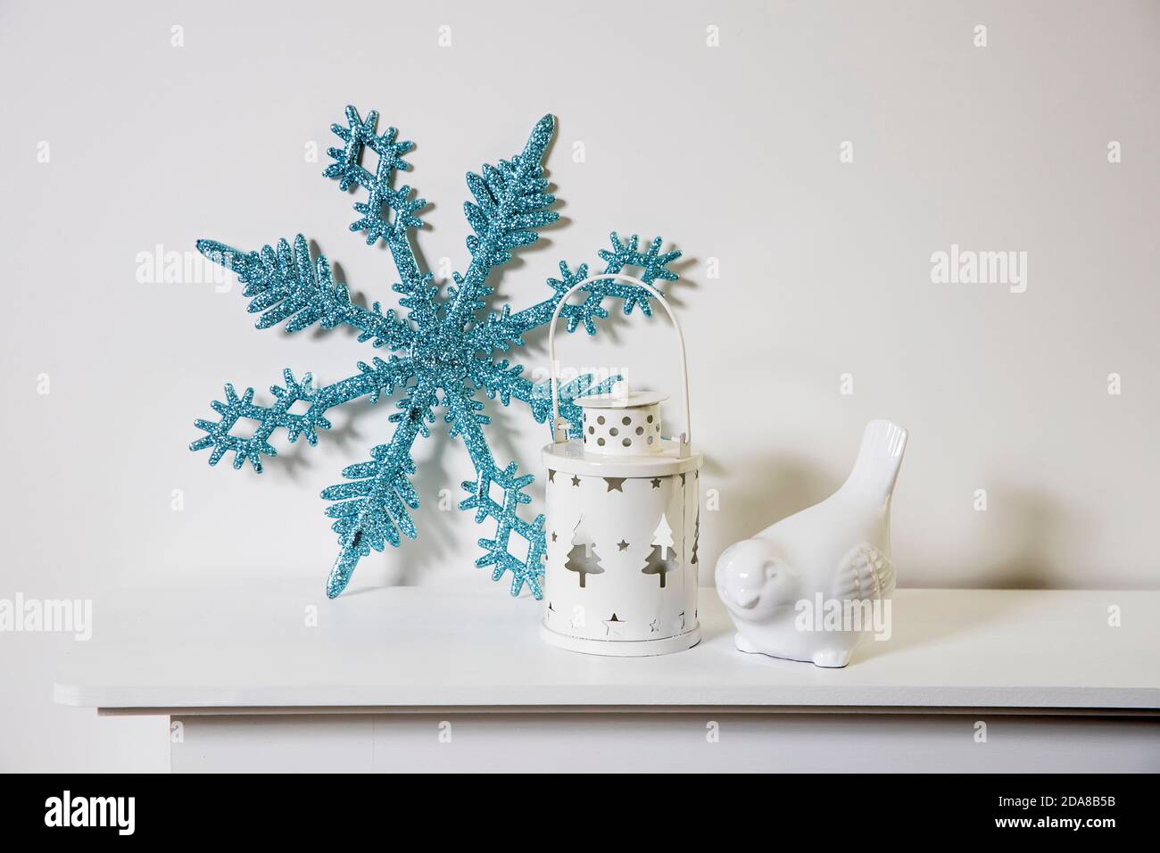 Décoration de Noël : flocon de neige bleu à paillettes artificielles, porte-bougie et porte-bougie en porcelaine blanc, figurine, bullfinch oiseau sur la console. Copier l'espace Banque D'Images